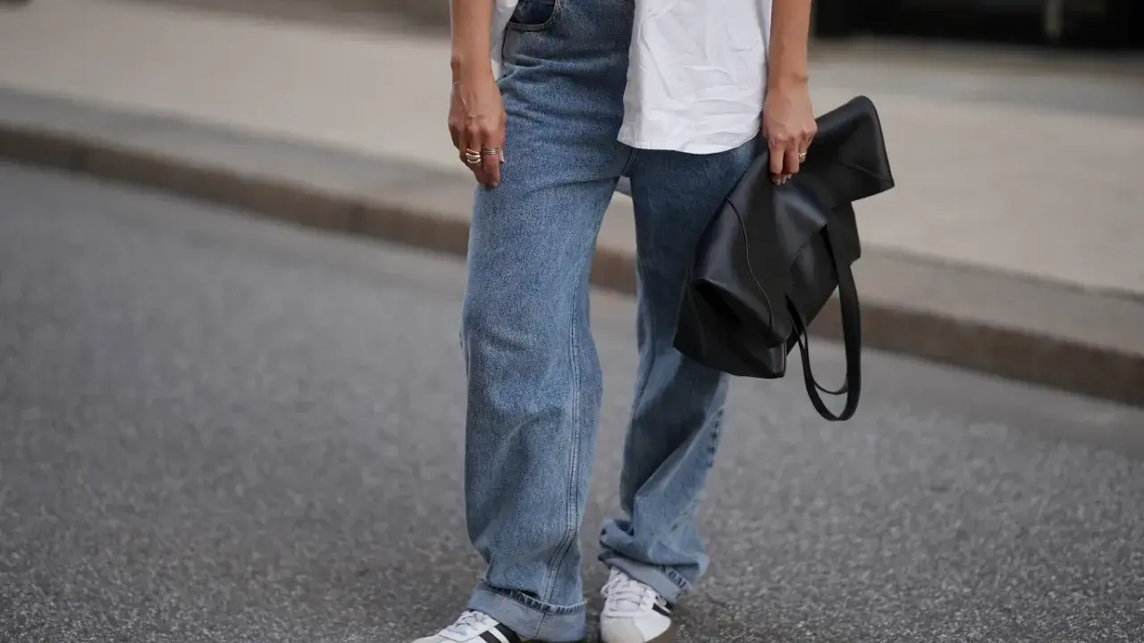 Modne jeansy flare w stylizacji z białą koszulą i czarną torebką.