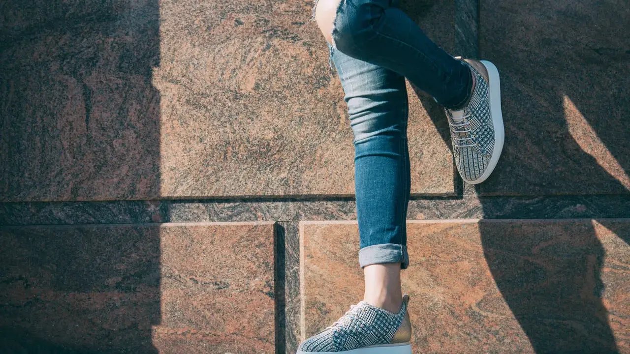 Kobieta w podartych jeansach i modnych sneakersach. Pokazano, jak podwinąć spodnie, by uzyskać stylowy efekt.