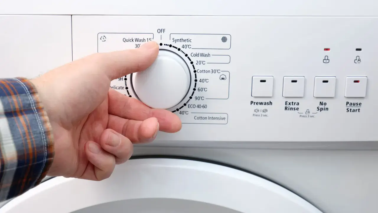 Dłoń ustawia pokrętło pralki. W ilu stopniach prac białe ubrania? Programy wskazują od 20°C do 90°C.