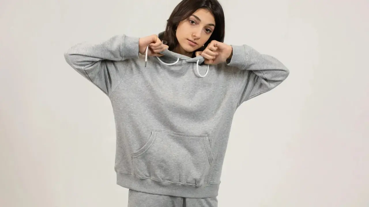 Dziewczyna w szarej bluzie z kapturem i spodniami dresowymi. Jej oversize styl podkreśla swobodę i komfort.