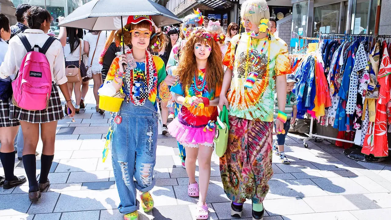 Kolorowy tłum w stylu harajuku, z tęczowymi ubraniami, dżinsowymi ogrodniczkami i jaskrawymi dodatkami, spaceruje ulicą.