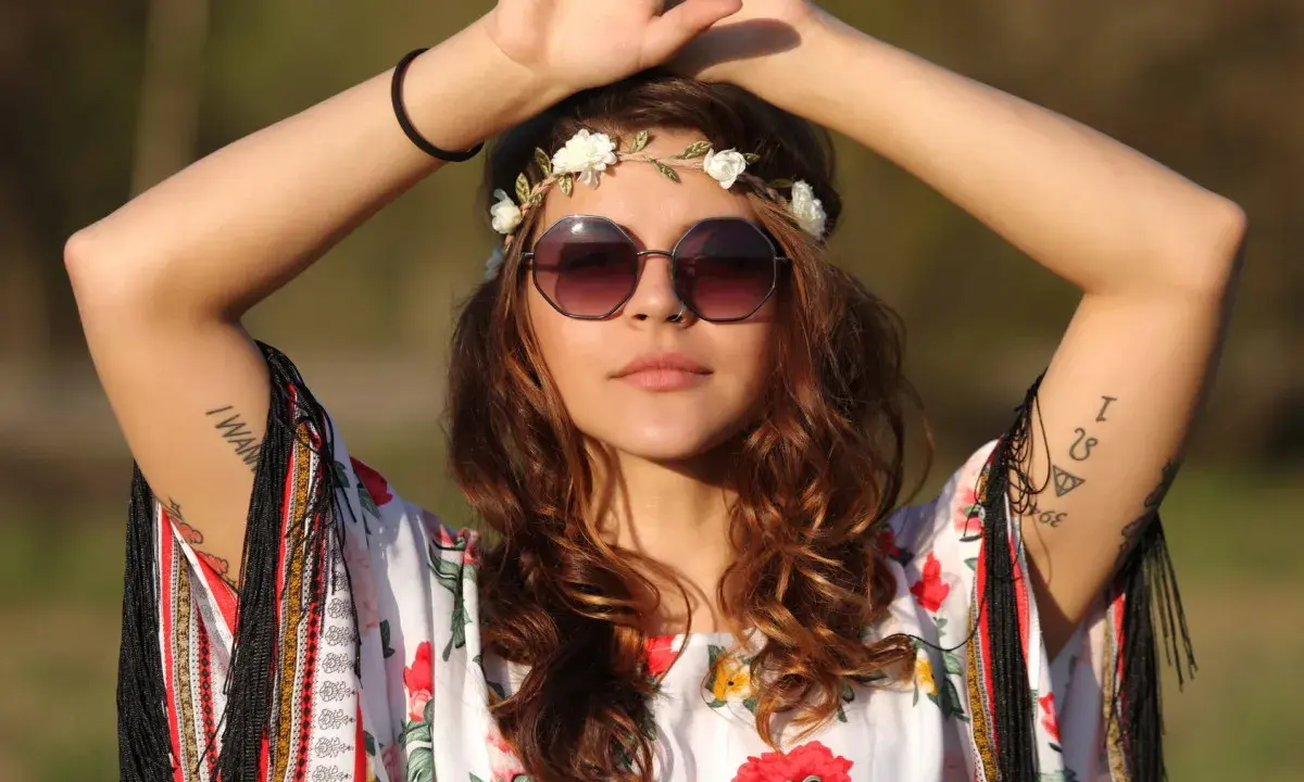 Dziewczyna w stylu boho, z wiankiem z kwiatów i okularami, w kwiecistej bluzce. Jej moda nawiązuje do wolności i natury, jak u dzieci kwiatów.