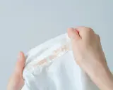 Dłoń trzyma białą bluzę z plamami podkładu. Zastanawiasz się, czym zmyć podkład z bluzy?
