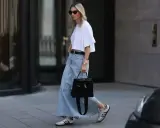 Kobieta w białej bluzce i długiej spódnicy jeansowej midi, z czarną torebką i sneakersami. Stylowe spódnica jeansowa midi stylizacje.