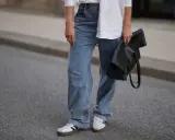 Modne jeansy flare w stylizacji z białą koszulą i czarną torebką.