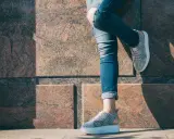 Kobieta w podartych jeansach i modnych sneakersach. Pokazano, jak podwinąć spodnie, by uzyskać stylowy efekt.