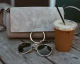 Zamszowa torebka Chloe, okulary i kawa na drewnianym stole. Dowiedz się, jak wyczyścić zamszową torebkę, by wyglądała jak nowa.