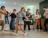 Luźne stylizacje na domówkę: jeansy, sukienka, spódniczka i sweter. Wszyscy tańczą i bawią się przy muzyce.