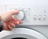 Dłoń ustawia pokrętło pralki. W ilu stopniach prac białe ubrania? Programy wskazują od 20°C do 90°C.