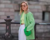 Kobieta w zielonej marynarce i topie typu **krój cropped co to znaczy** – odsłaniający brzuch. W ręku trzyma zieloną torebkę.