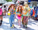 Kolorowy tłum w stylu harajuku, z tęczowymi ubraniami, dżinsowymi ogrodniczkami i jaskrawymi dodatkami, spaceruje ulicą.