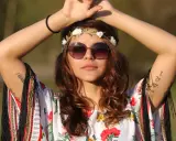 Dziewczyna w stylu boho, z wiankiem z kwiatów i okularami, w kwiecistej bluzce. Jej moda nawiązuje do wolności i natury, jak u dzieci kwiatów.