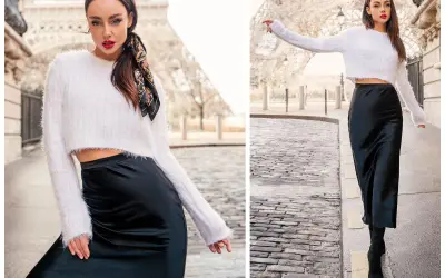 Kobieta w białym sweterku i czarnej satynowej spódnicy, uosobienie stylu minimalistycznego mody, pozuje na tle Wieży Eiffla.