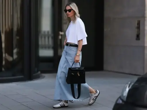Kobieta w białej bluzce i długiej spódnicy jeansowej midi, z czarną torebką i sneakersami. Stylowe spódnica jeansowa midi stylizacje.