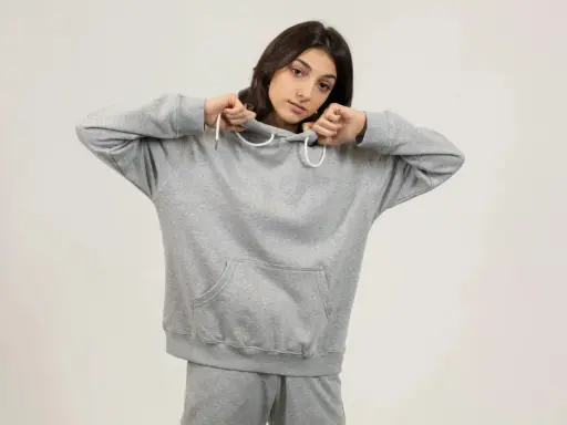 Dziewczyna w szarej bluzie z kapturem i spodniami dresowymi. Jej oversize styl podkreśla swobodę i komfort.