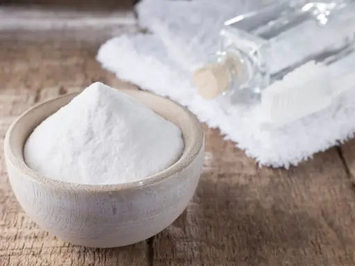 Biała soda w drewnianej miseczce, obok buteleczka z płynem i szczoteczka. Idealne do usuwania plam i jako soda na zafarbowane ubrania.