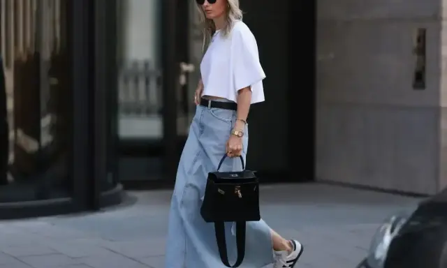 Kobieta w białej bluzce i długiej spódnicy jeansowej midi, z czarną torebką i sneakersami. Stylowe spódnica jeansowa midi stylizacje.