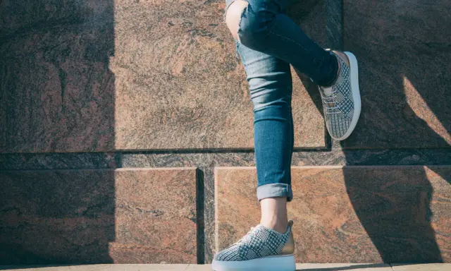 Kobieta w podartych jeansach i modnych sneakersach. Pokazano, jak podwinąć spodnie, by uzyskać stylowy efekt.
