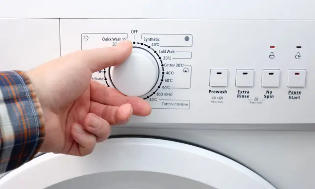 Dłoń ustawia pokrętło pralki. W ilu stopniach prac białe ubrania? Programy wskazują od 20°C do 90°C.