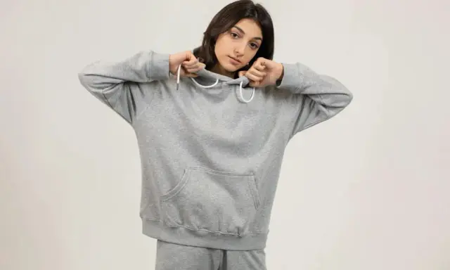 Dziewczyna w szarej bluzie z kapturem i spodniami dresowymi. Jej oversize styl podkreśla swobodę i komfort.