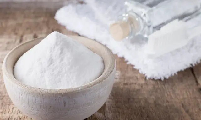 Biała soda w drewnianej miseczce, obok buteleczka z płynem i szczoteczka. Idealne do usuwania plam i jako soda na zafarbowane ubrania.