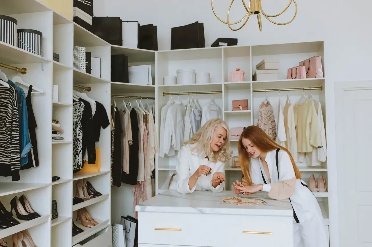 Dwie kobiety przeglądają biżuterię w garderobie w stylu minimalistycznym moda. Ubrania i buty schludnie poukładane.