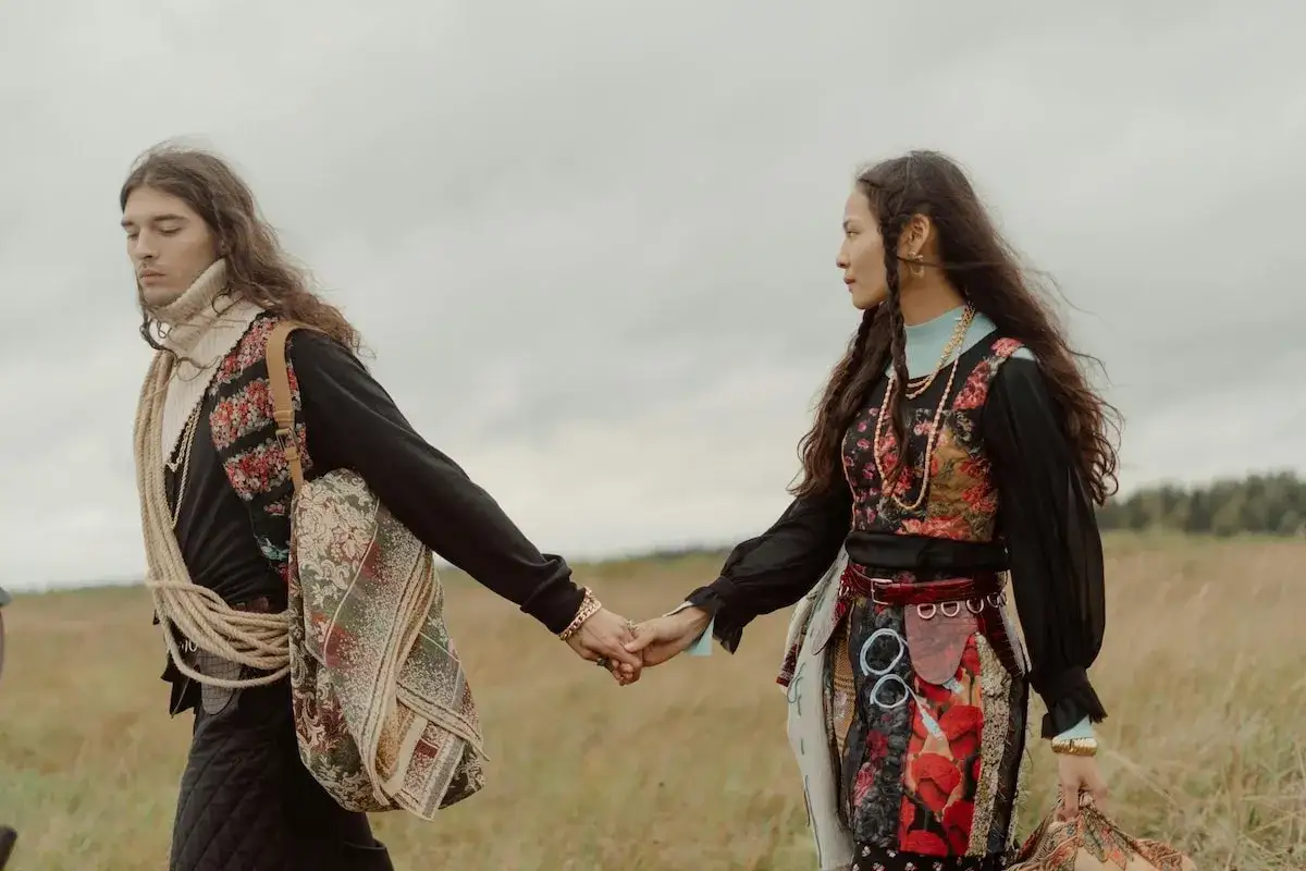 Para idzie przez łąkę, trzymając się za ręce. Ich styl to boho, z motywami kwiat&oacute;w i dziecięcej swobody. Moda inspirowana naturą.